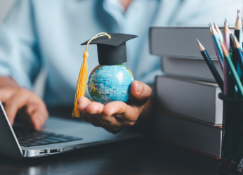 Student with books and laptop holding small globe with grad cap