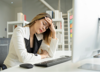Woman sitting at work computer holding her forehead